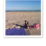 Yogamatta, sandstrand, havet, rosa Converse-skor och vattenflaskor.