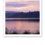 Vy över en sjö en stilla sommarkväll, med en himmel i rosa.